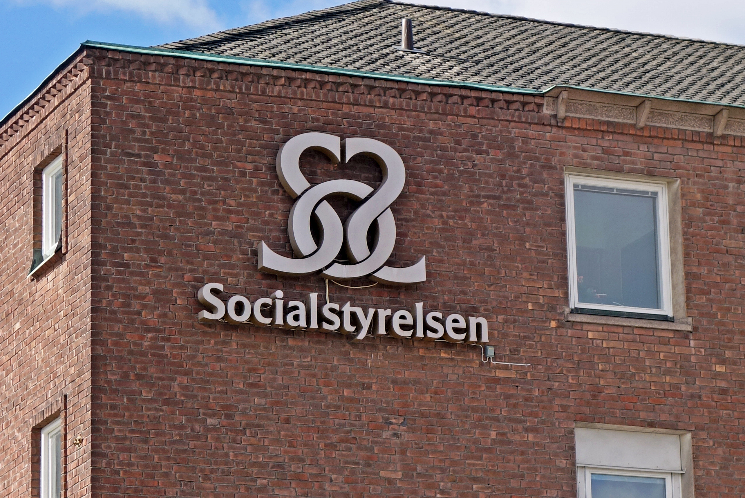 En byggnad i tegel har en skylt med logotyp och texten "Socialstyrelsen" på ytterväggen.