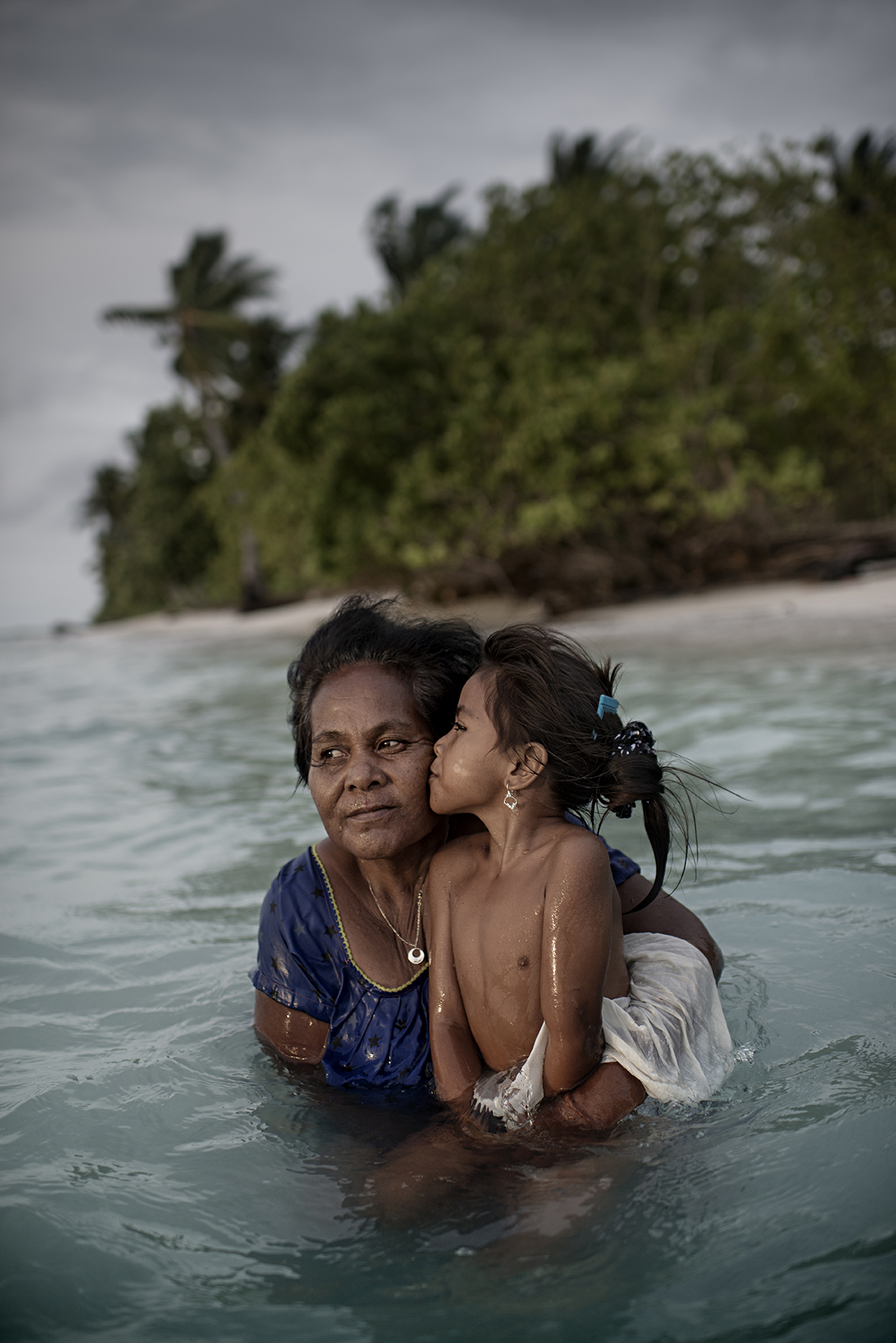 Bwebwe Nakorini och hennes dotter Rini står i vattnet utanför deras hus i Buariki. Tidigare nådde stranden ut hit.