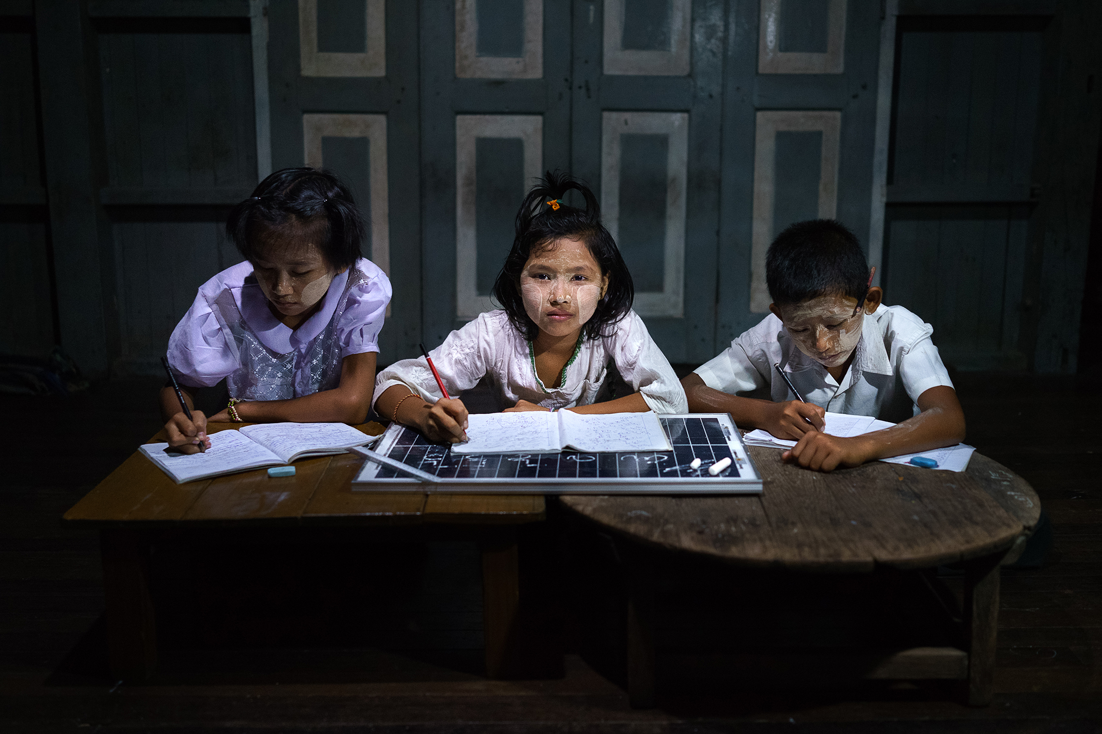 Burmesiska grundskoleelever gör läxan på sitt solcellsupplysta fritids i stadsdelen Dala i utkanten av storstaden Rangoon.