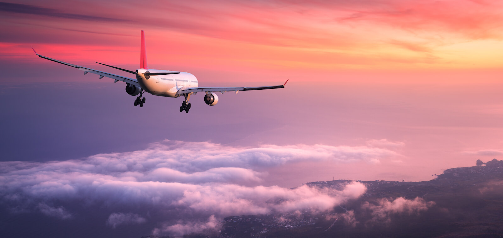 Flygplan i solnedgång flyger över hav och en kuststräcka.