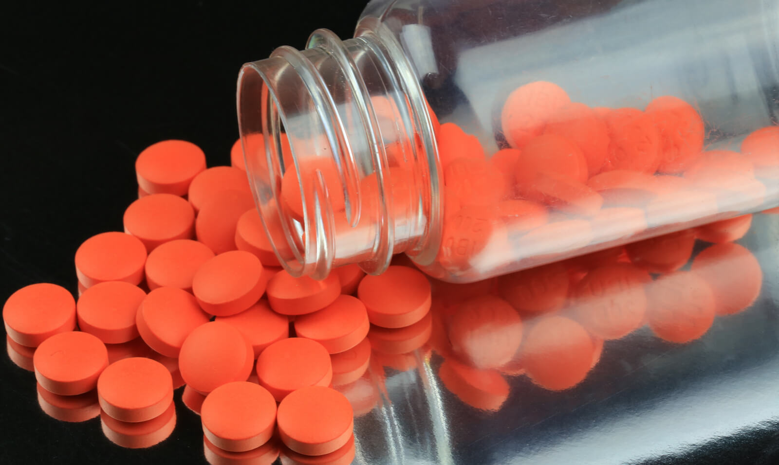 Röda piller i en glasburk på ett svart bord.