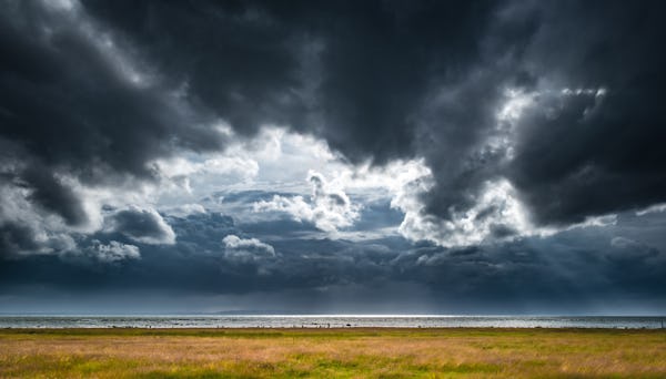 Mörka moln över hav och ängsstrand.