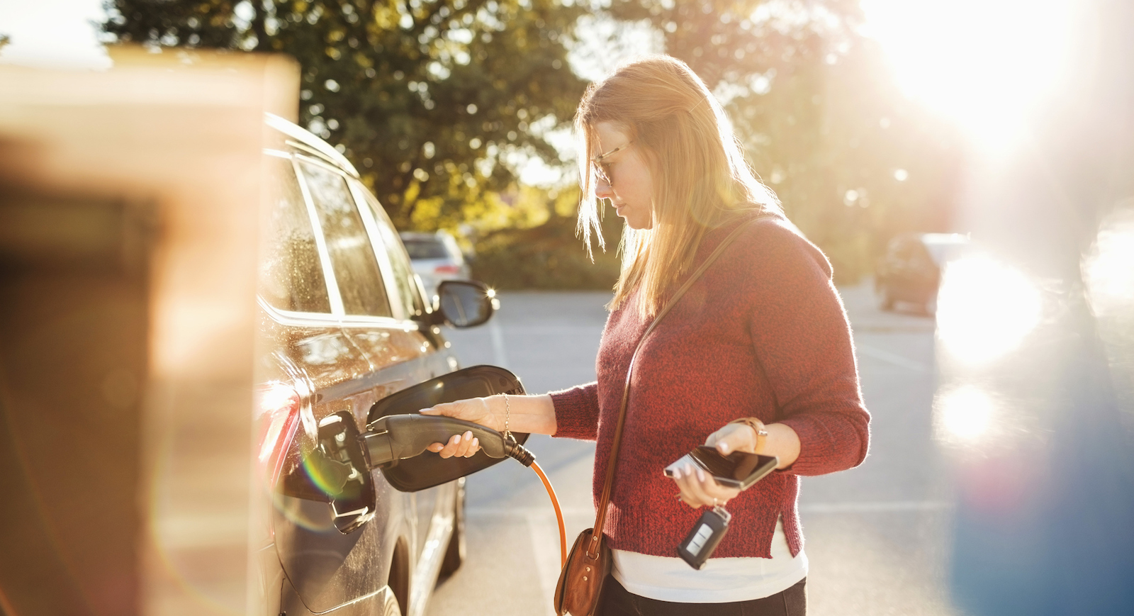 Kvinna laddar en elbil med sol i bakgrunden.