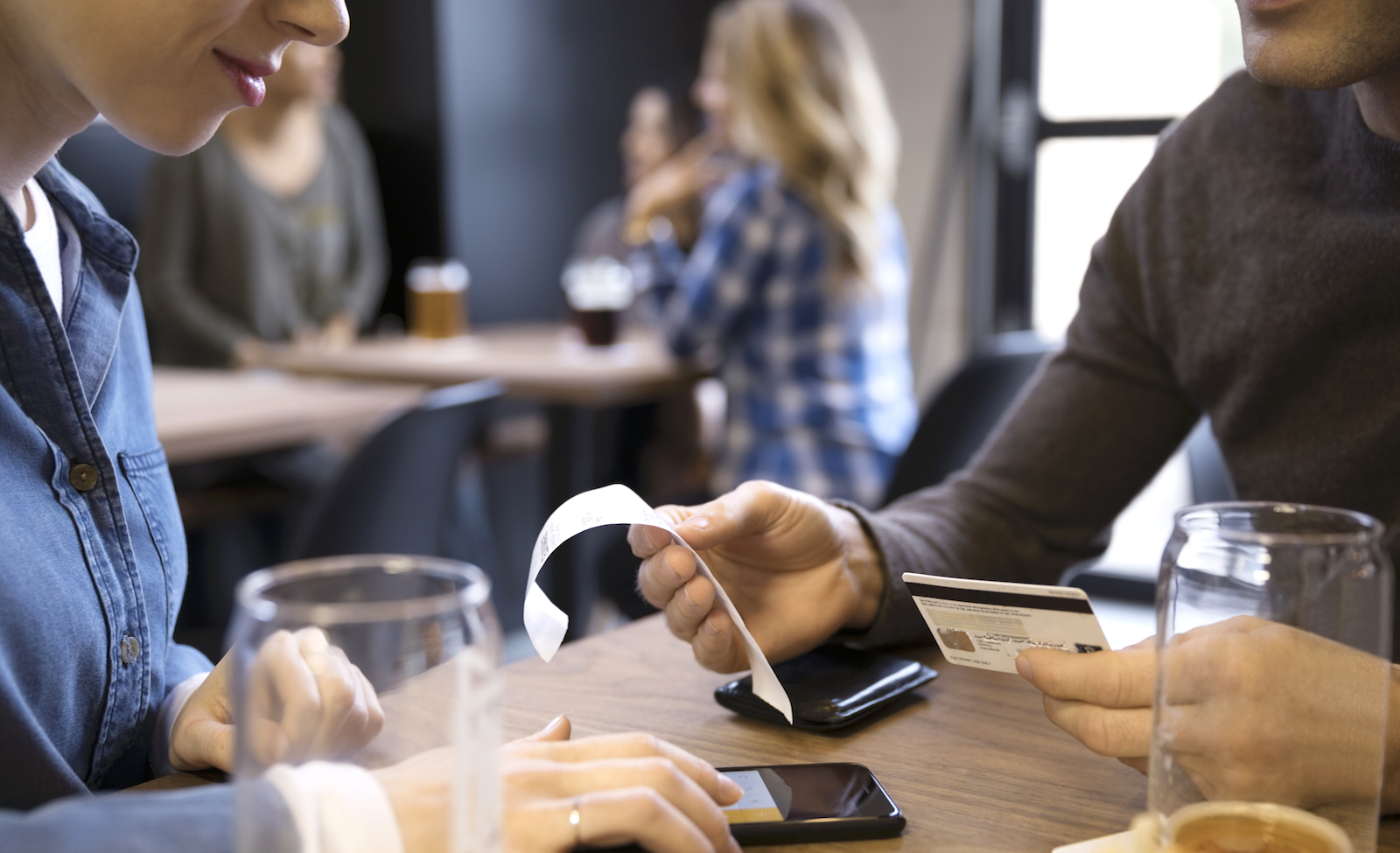 Par delar på notan på en restaurang. En man håller upp ett kvitto medan en kvinna räknar ut en summa på mobiltelefonen.