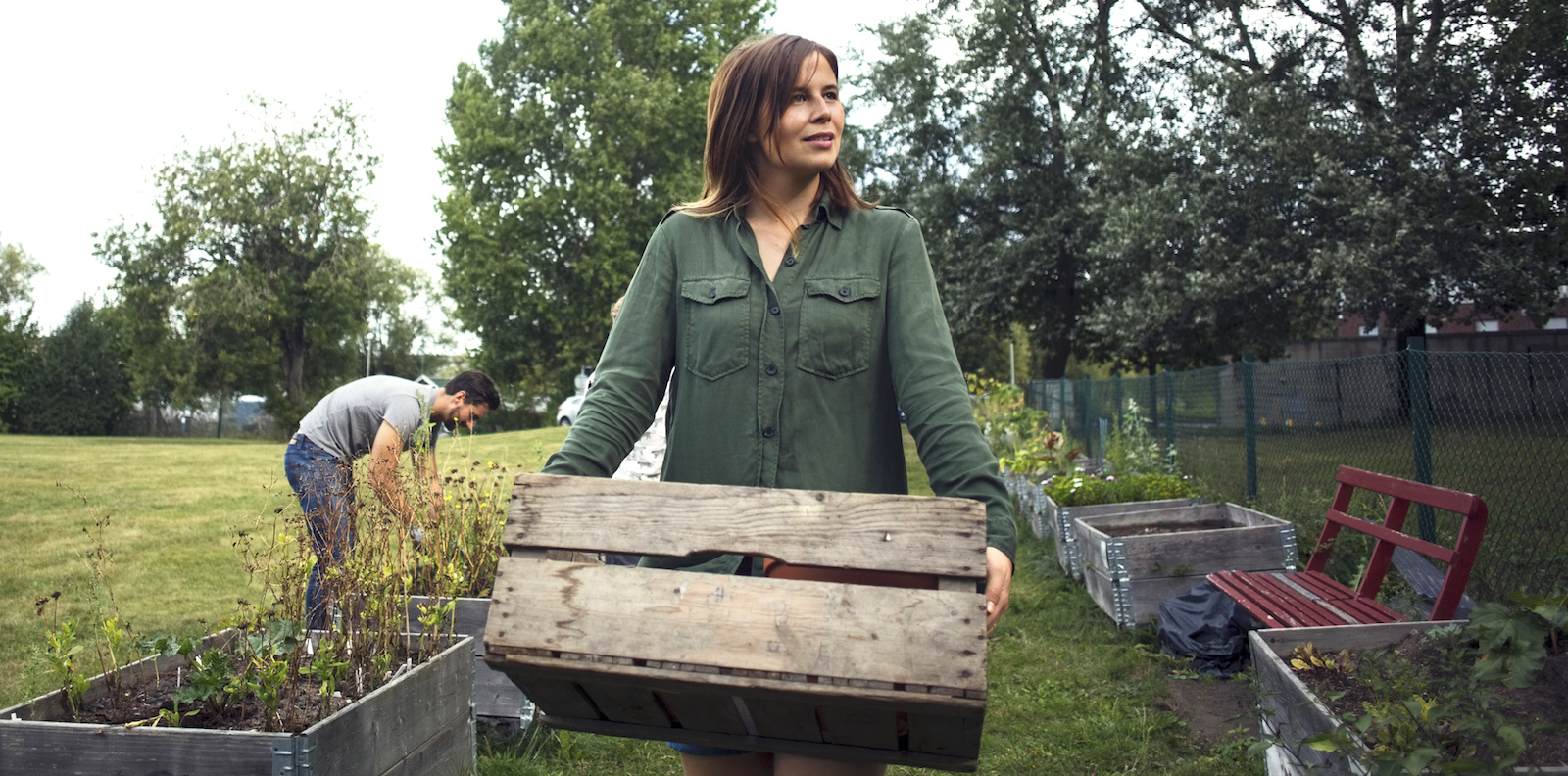 Kvinna bär en lastpall. En man i bakgrunden påtar i jorden.