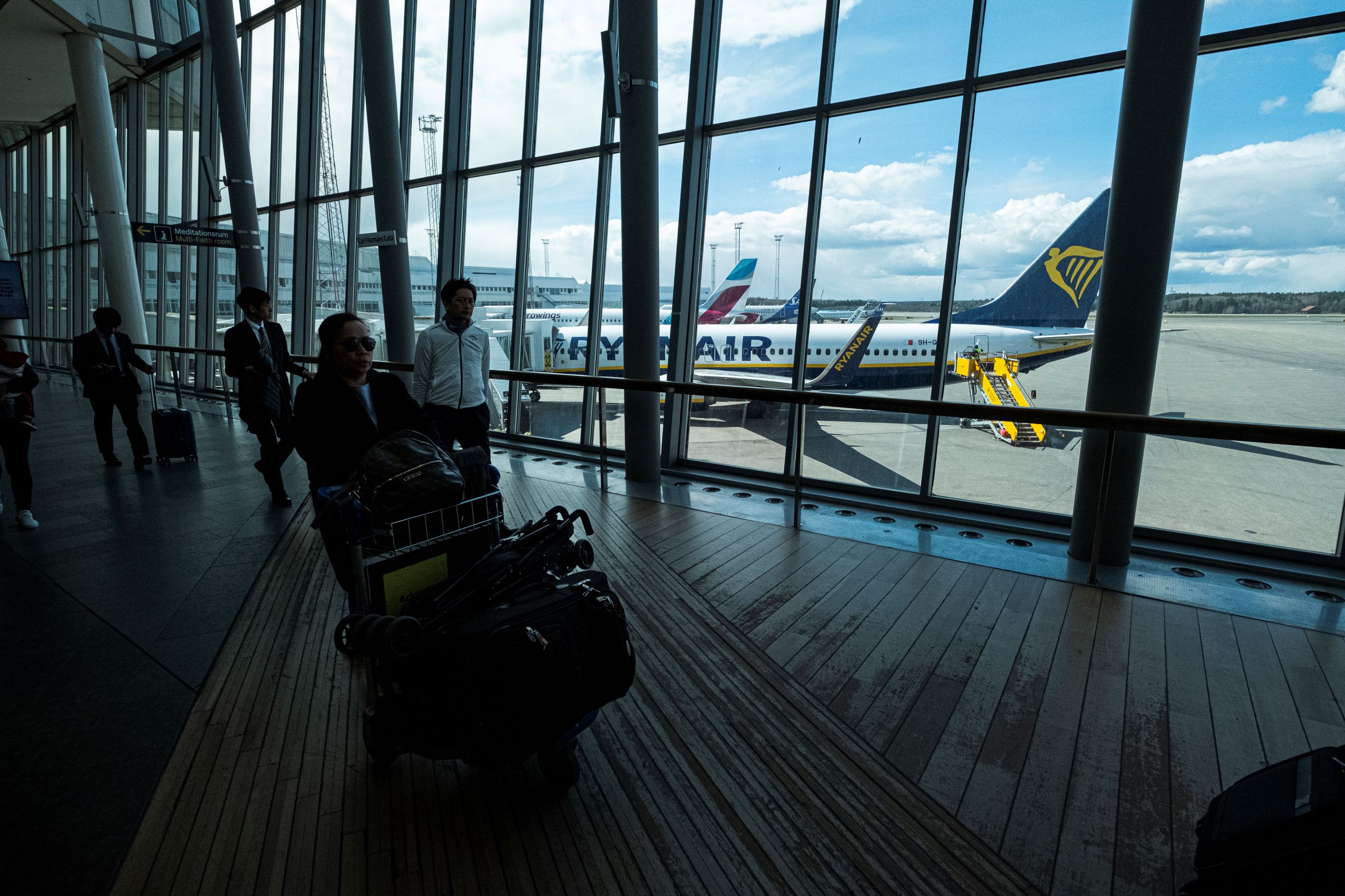 Passagerar på flygterminal med flygplan utanför fönstret.