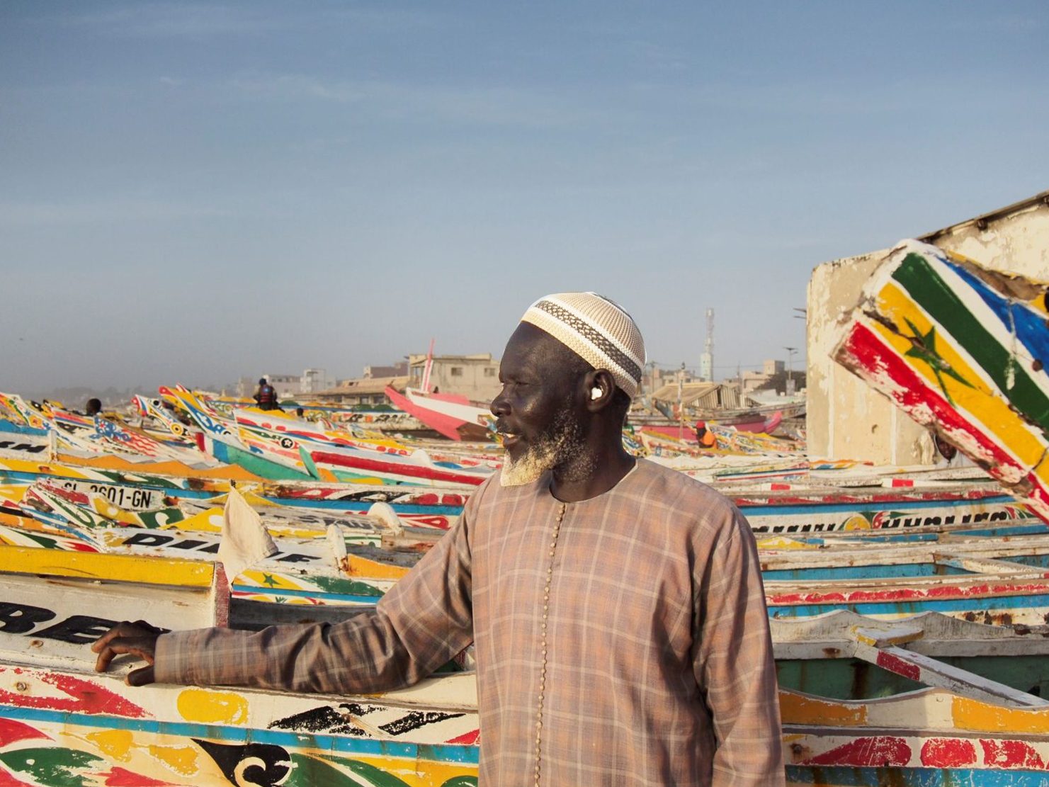 Man framför färgglada båtar på strand i Senegal.