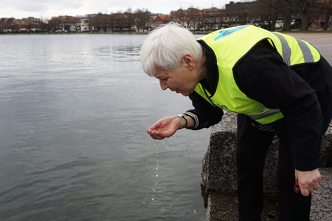 Kvinna i gul väst dricker vatten ur sjö.
