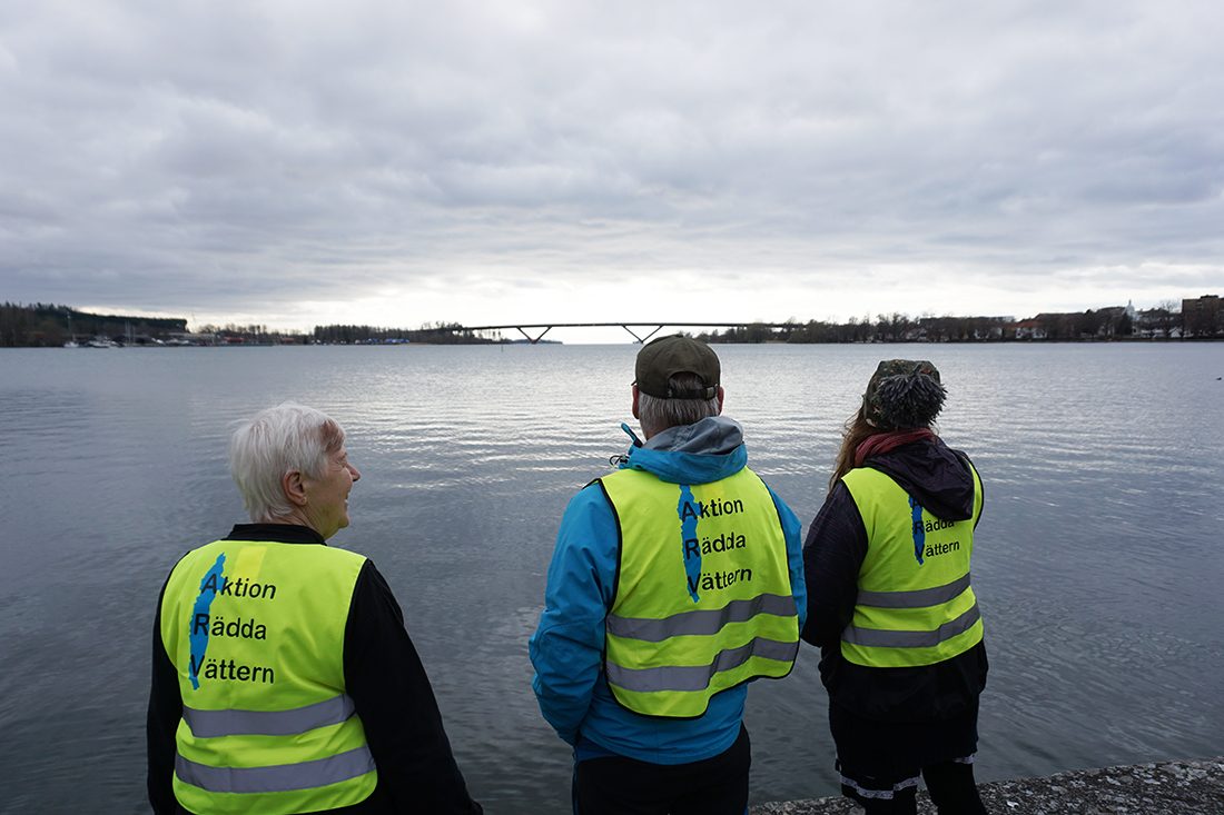 tre personer i gula västar vid vatten