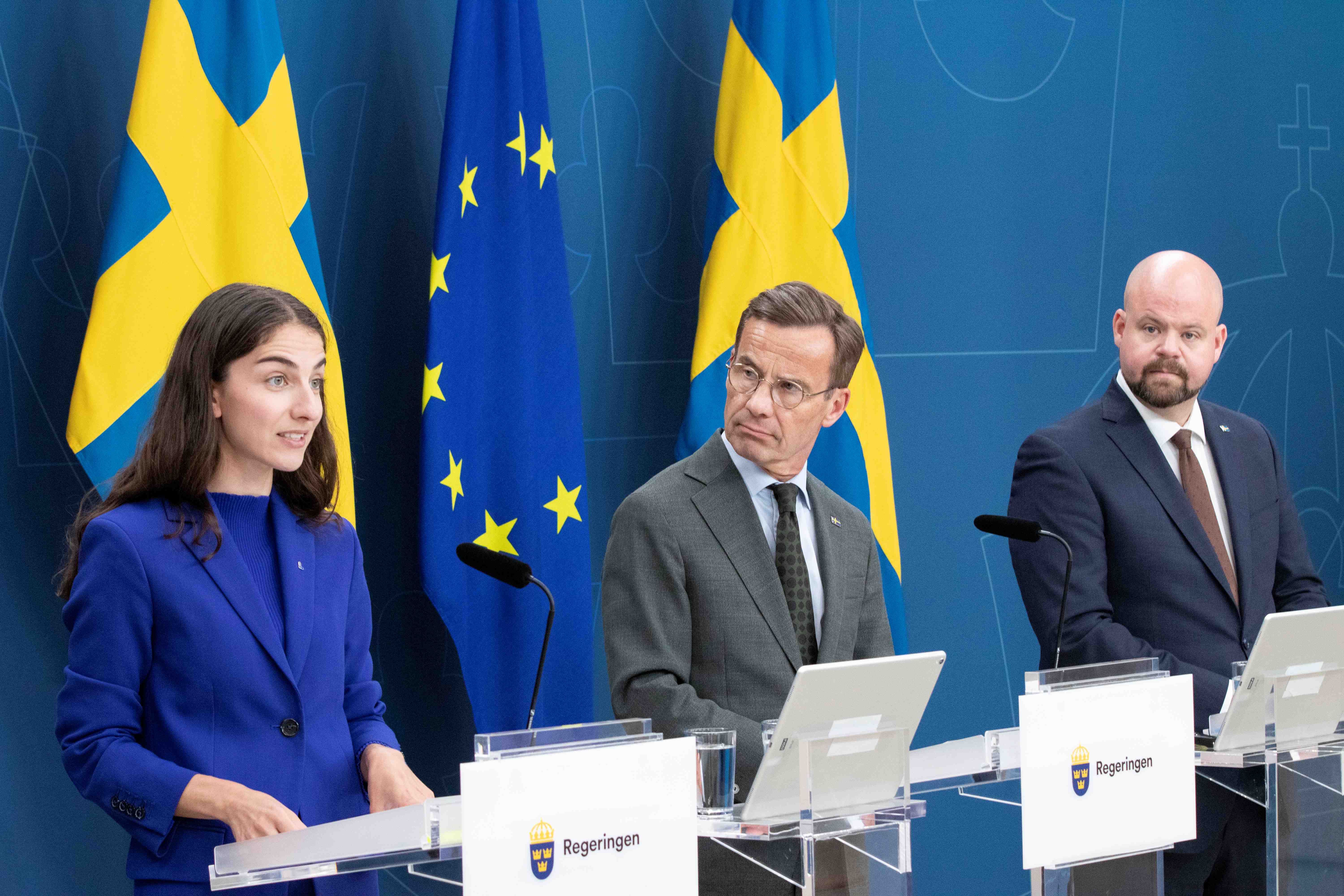 Kvinna i dräkt med två män i kostym vid flaggor