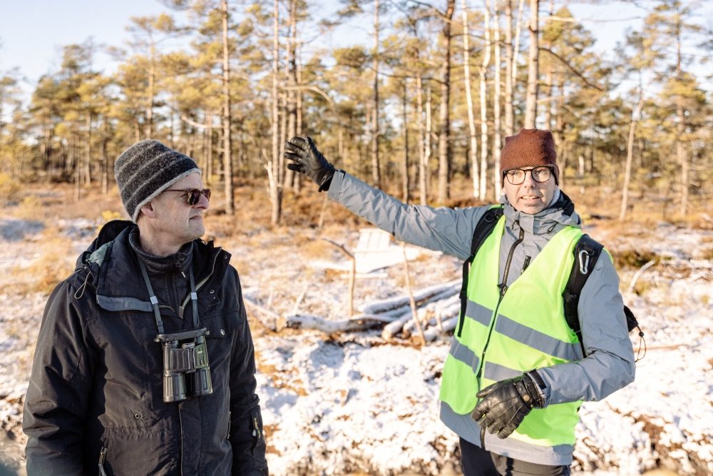 Män med mössor och varma kläder på snötäckt mosse.
