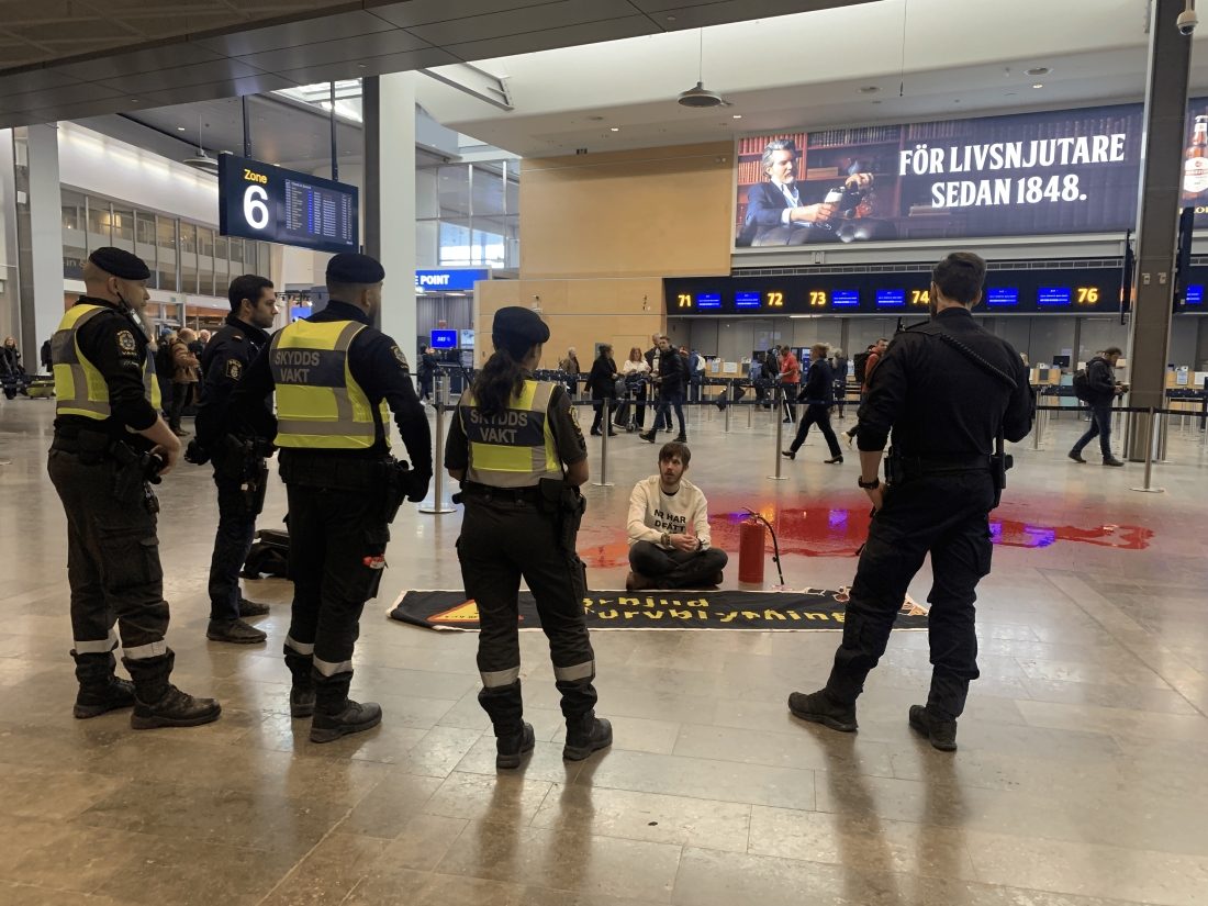 Klimataktivist på golv med röd färg, framför polis och ordningsvakter.