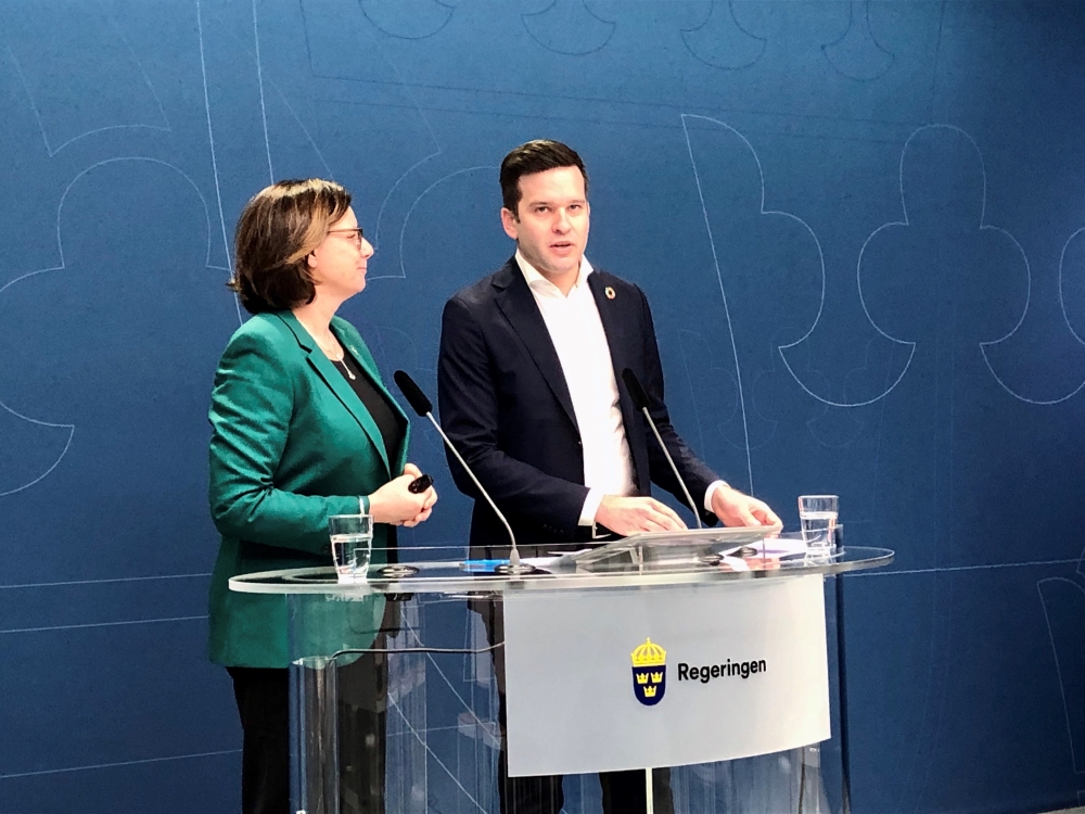 Kvinna i dräkt och man i kostym vid podium.