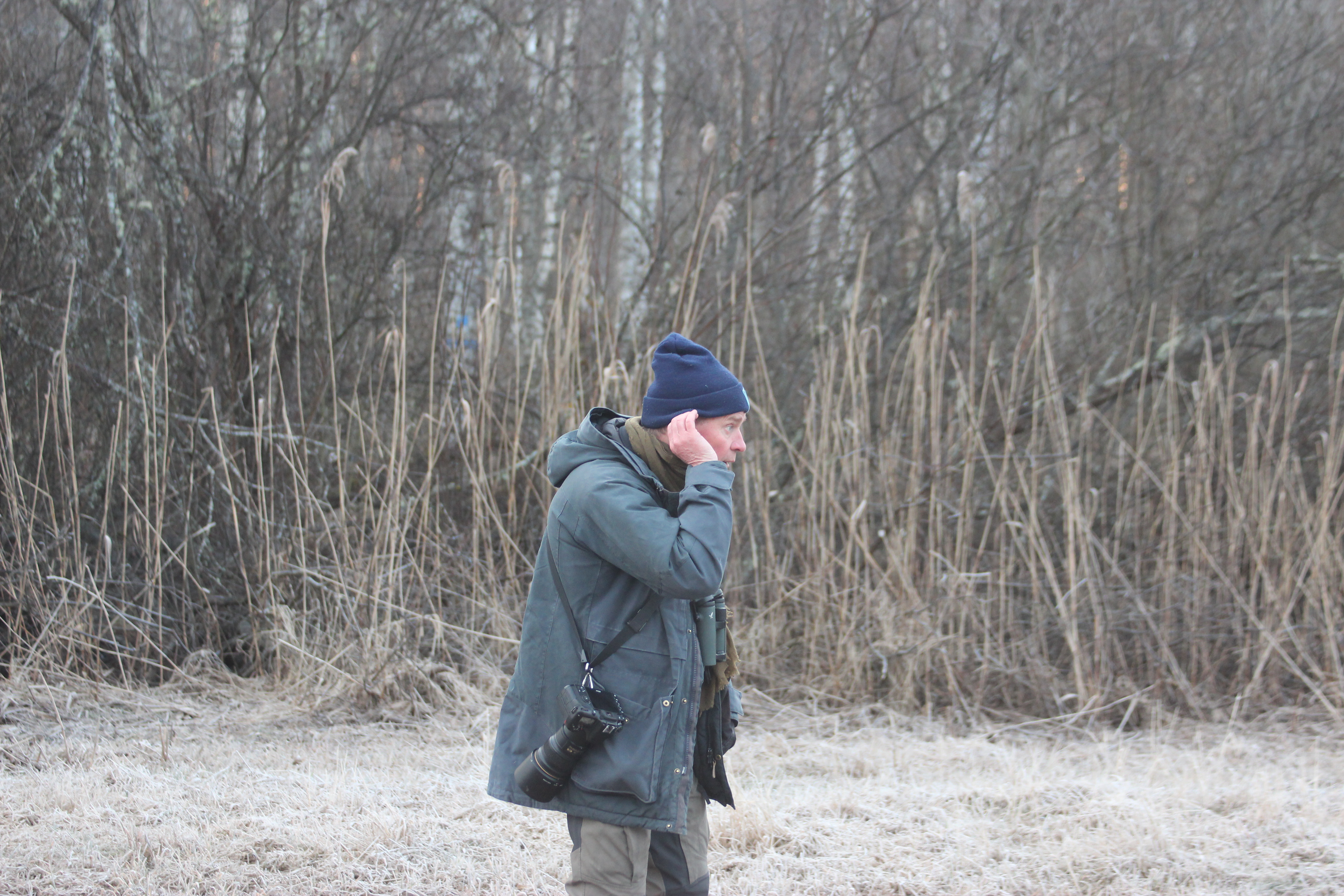 En man står och lyssnar med handen kupad bakom örat.