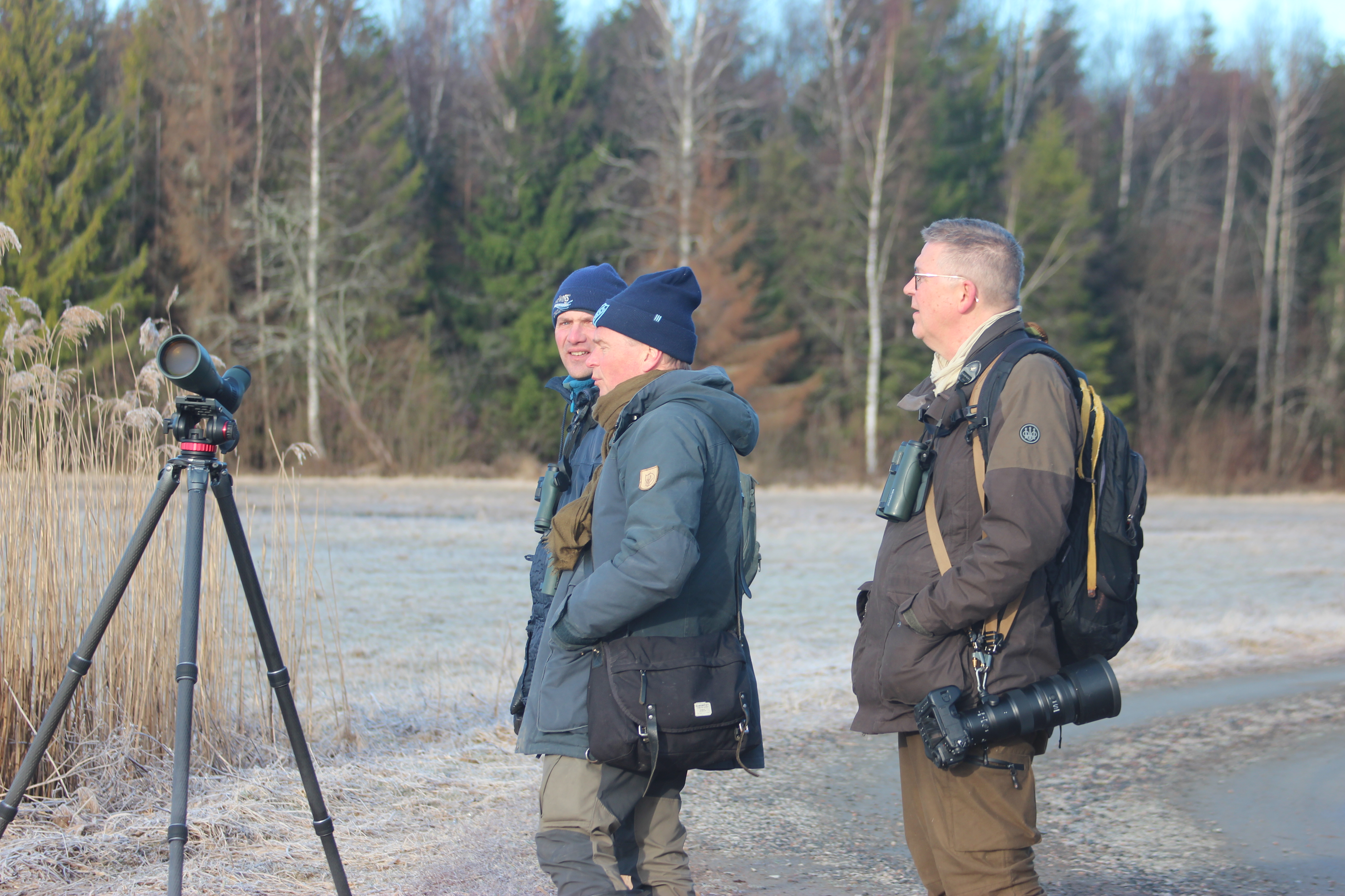 Tre män står bredvid en kikare på en åker.