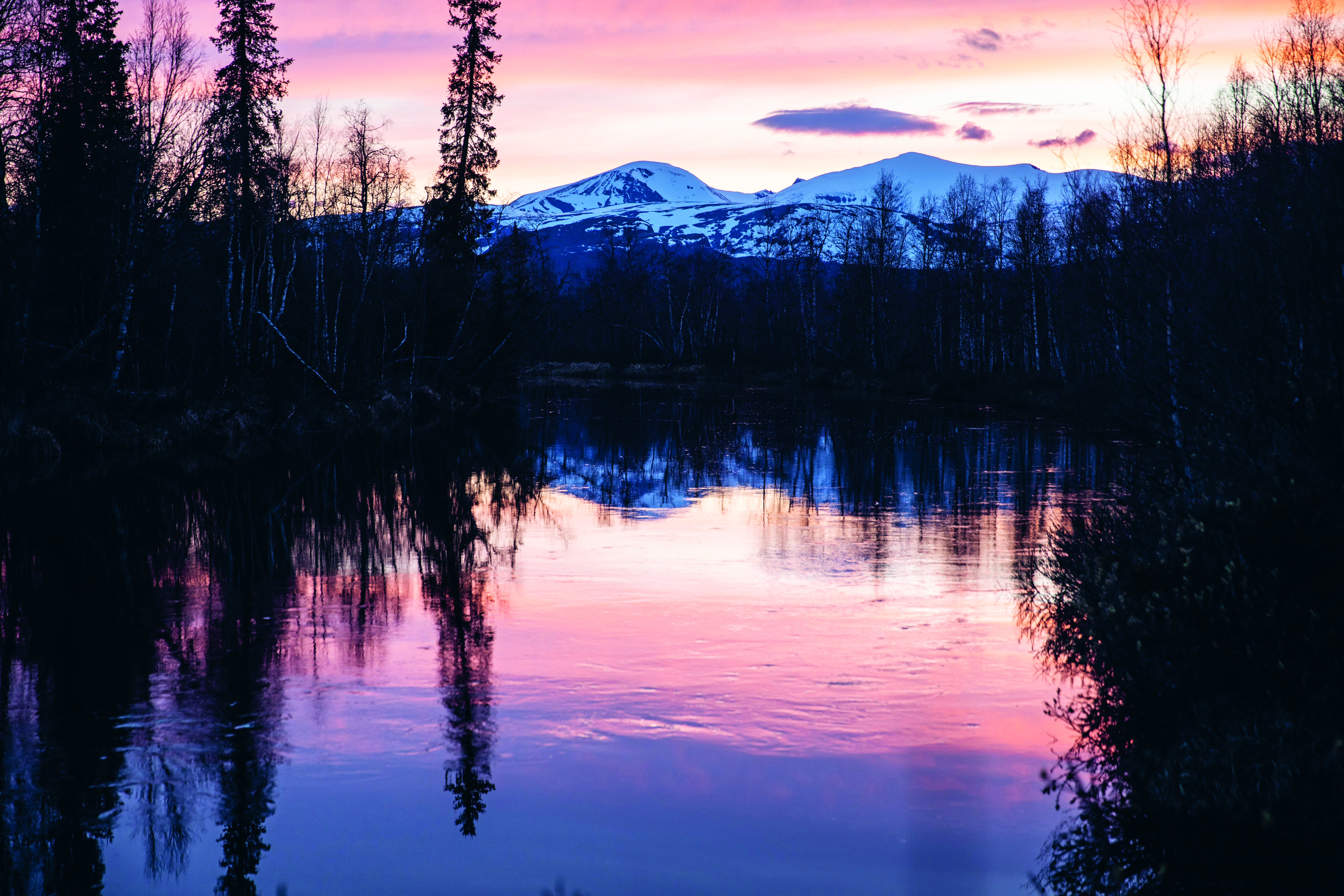 Skymning över fjällsjö med berg i horisonten.