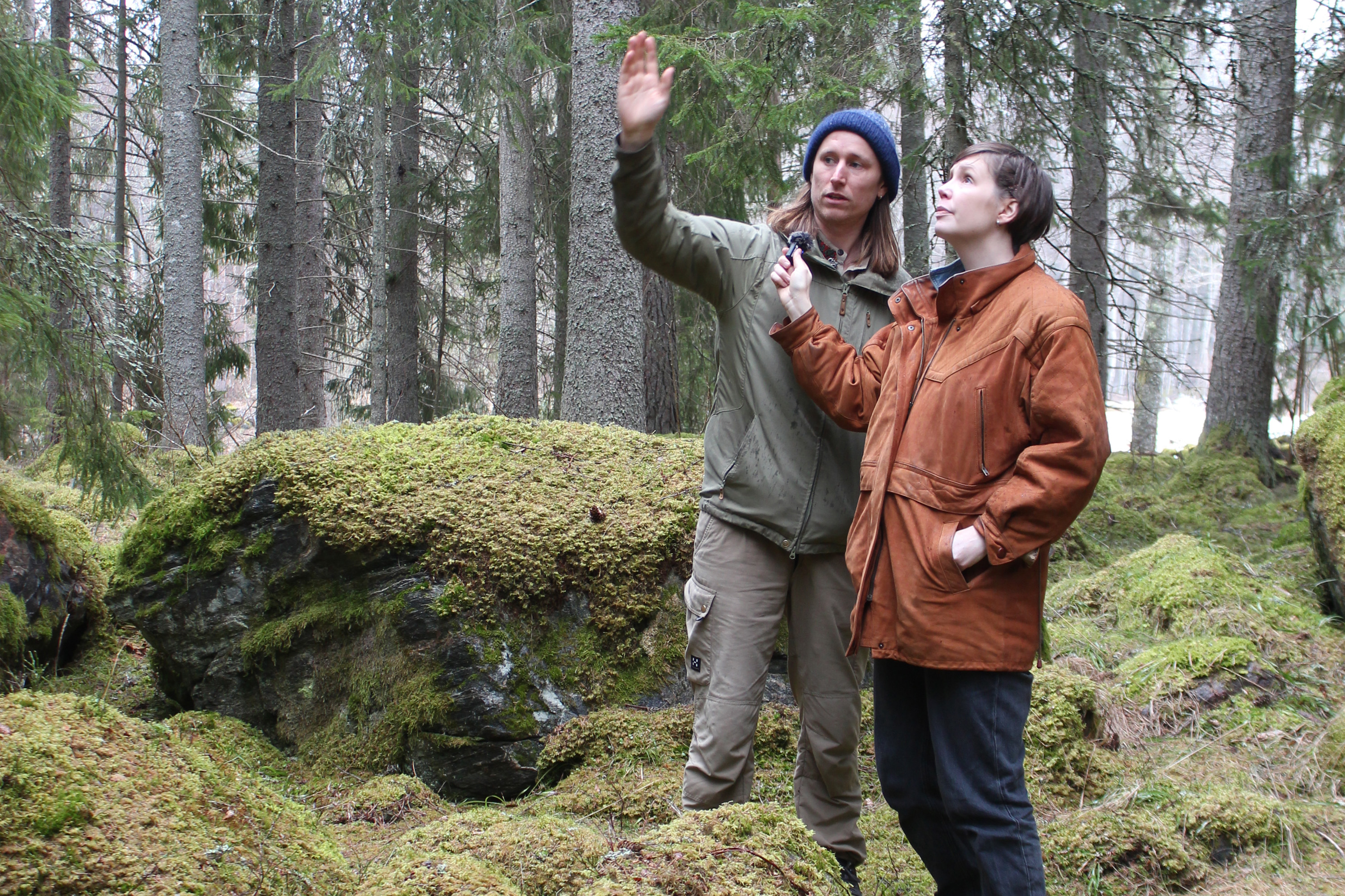 Två personer står i skog och den ena intervjuar den andra.