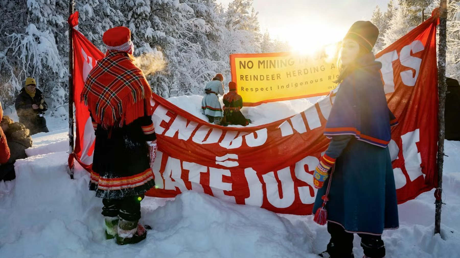 Människor i samiska kläder protesterar mot en gruva med banderoller i vinterlandskap.