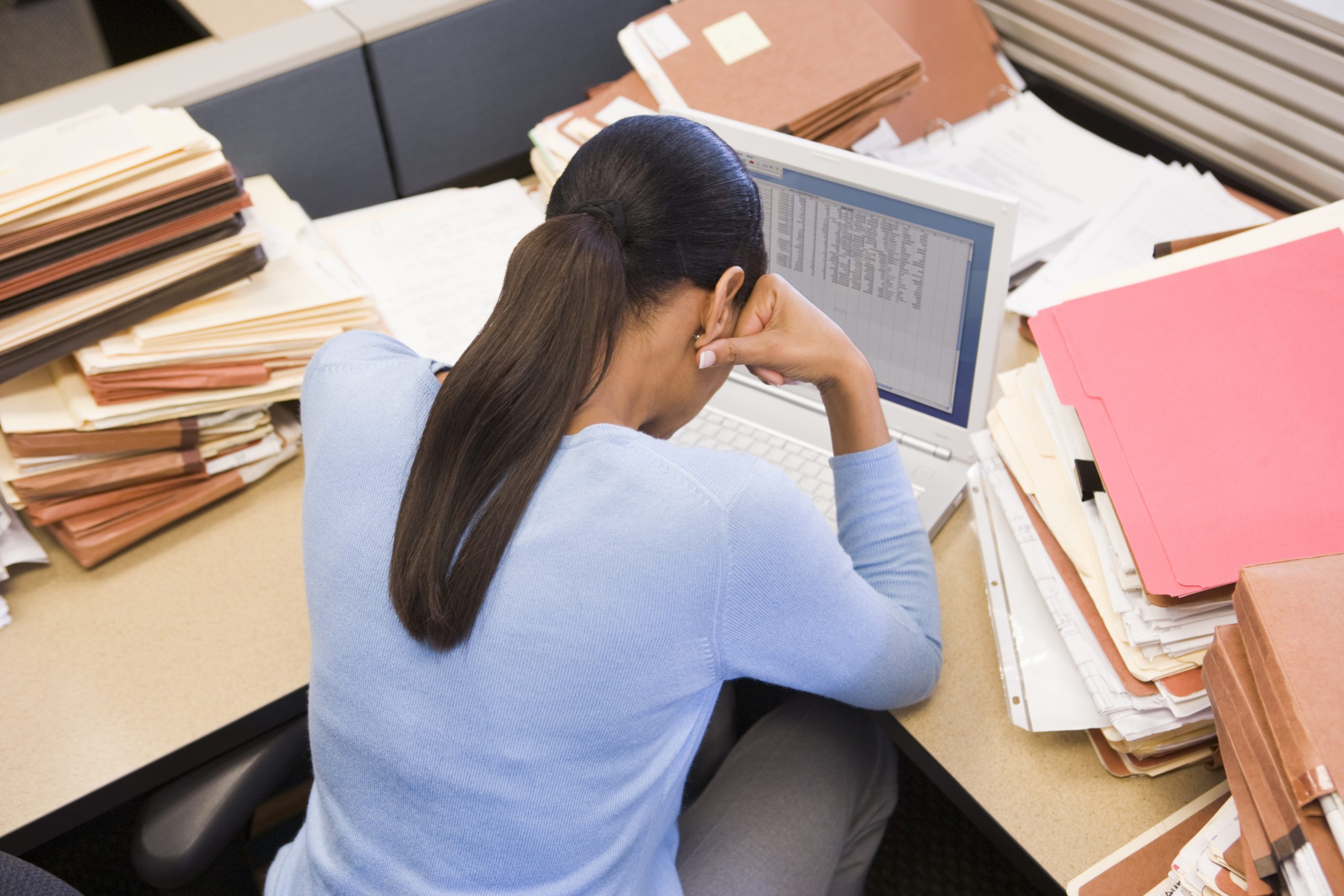 2161107-businesswoman-in-cubicle-with-laptop-and-stacks-of-files