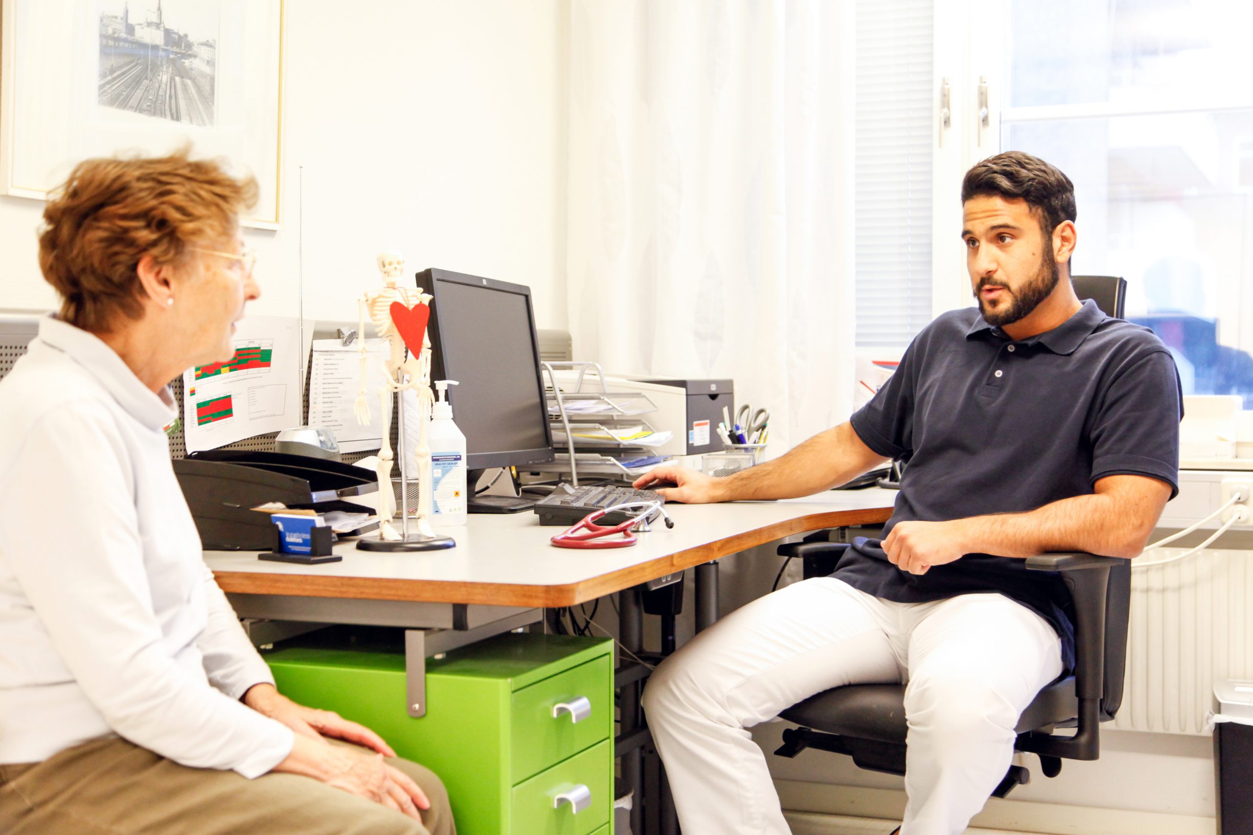 En ung manlig läkare samtalar med en äldre kvinnlig patient. 