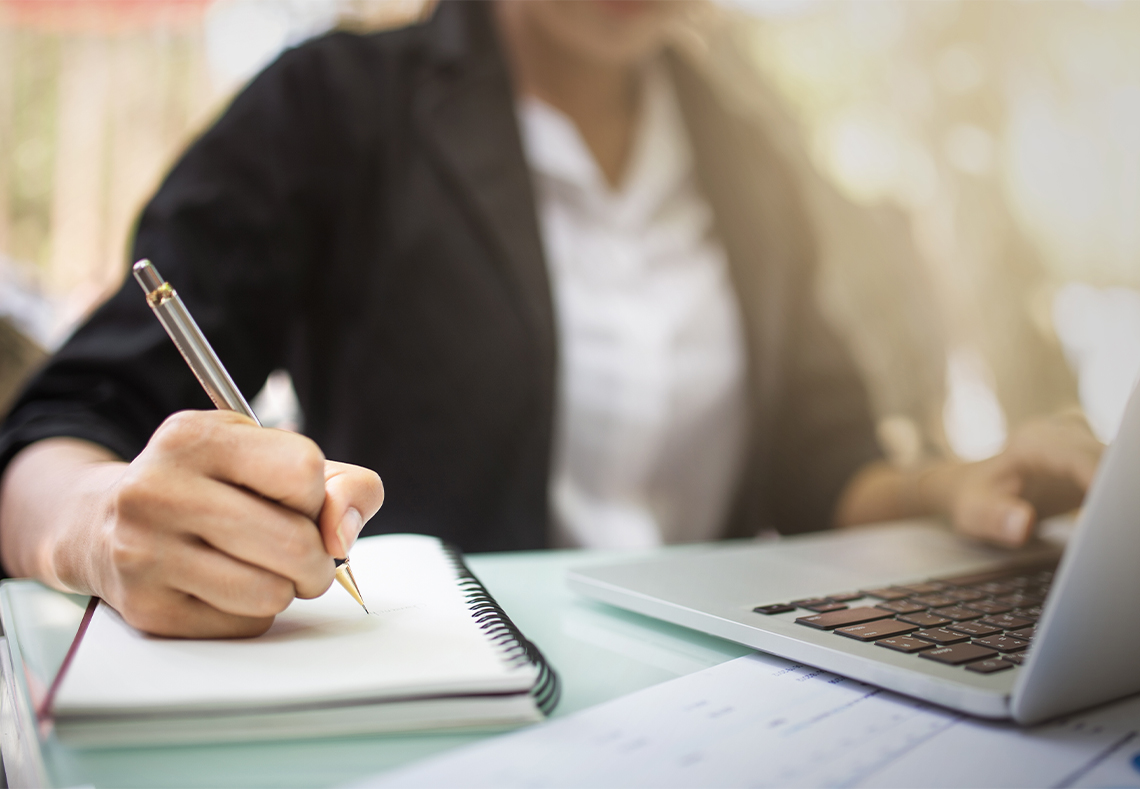 Person med dator och anteckningsblock som studerar/jobbar.