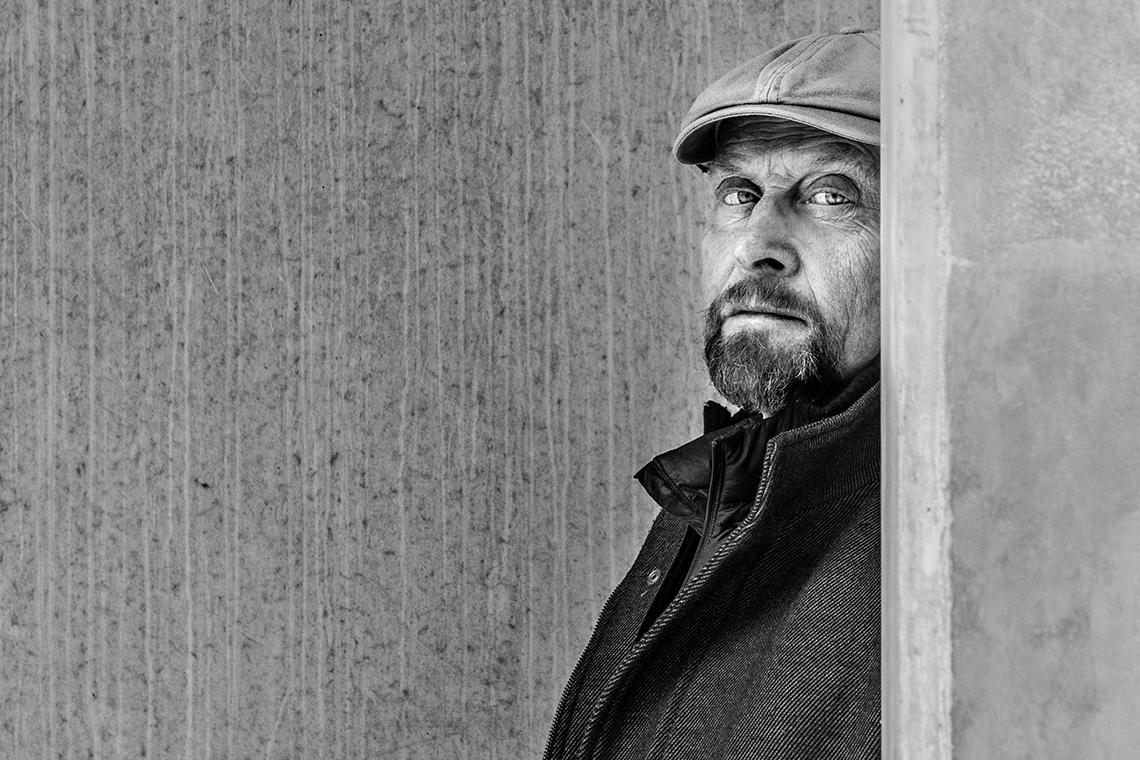Man med keps står framför en betongvägg.