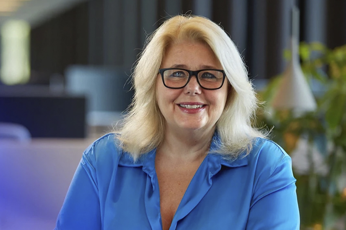 Leende blond kvinna i svarta glasögon och ljusblå sidenblus.