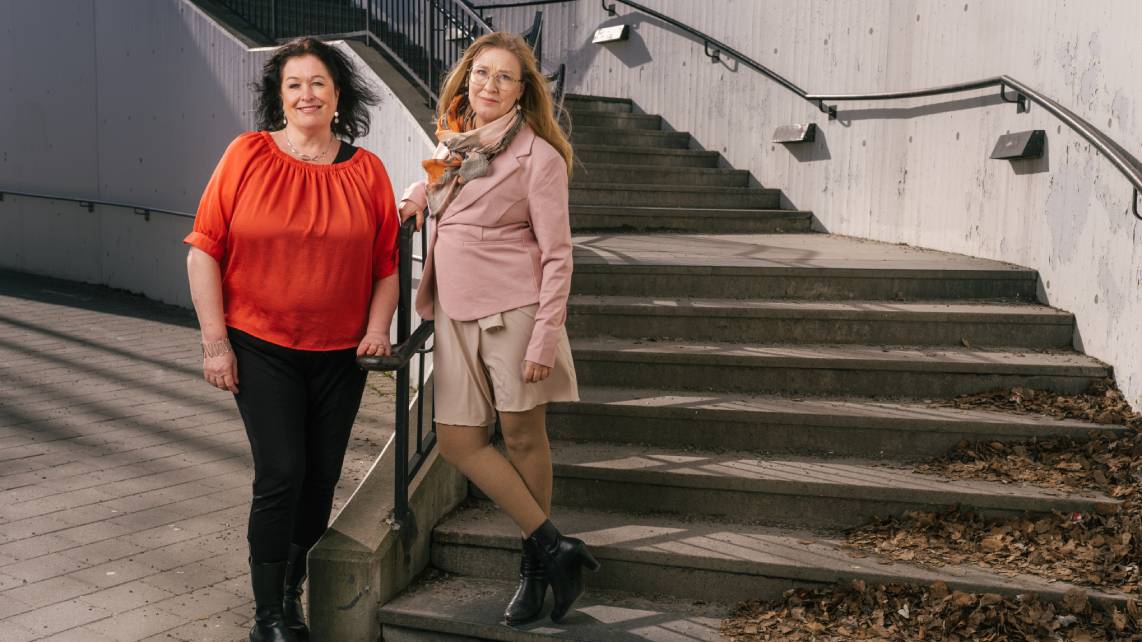 Två kvinnor står utomhus vid en stentrappa.