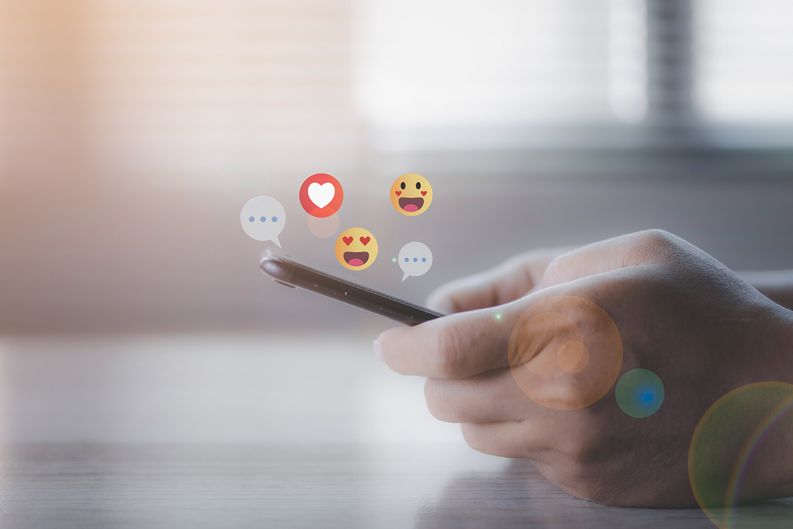 Hand som håller i en mobiltelefon och illustrerade emojis