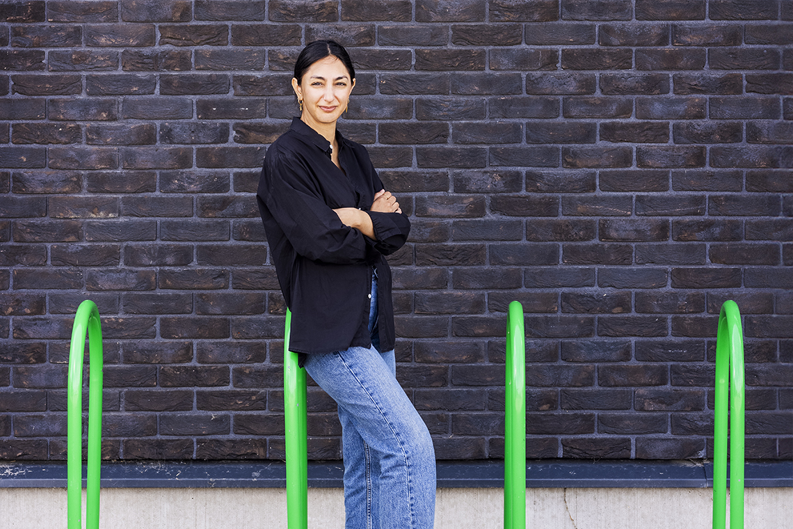 Seher Yilmaz, klädd i svart skjorta och jeans, står lutad mot ett knallgrönt cykelställ.