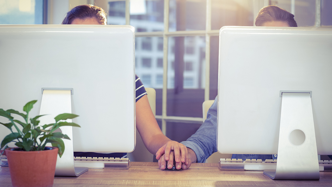 Två personer som håller hand skymda bakom datorskärmar.