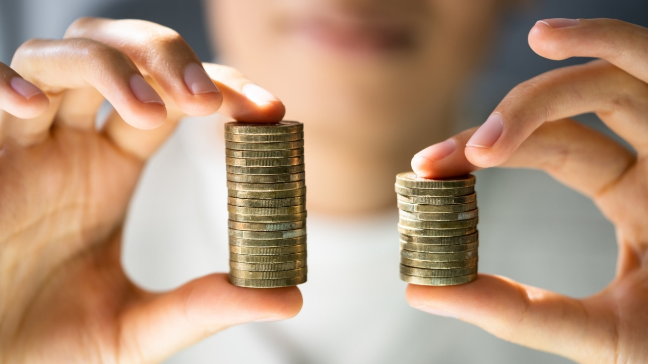En person som håller upp två högar med mynt som är olika höga för att illustrera artikeln om löneskillnader mellan män och kvinnor i Sverige.