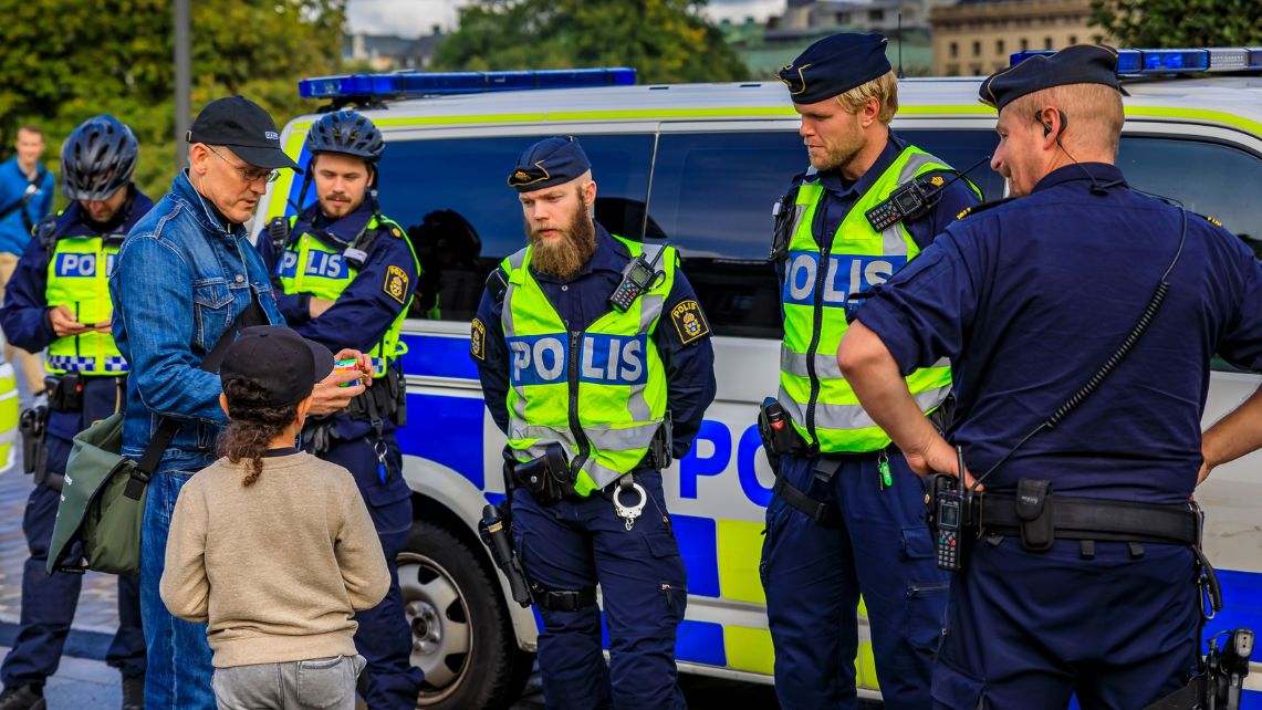 Polispatrull pratar med äldre man och litet barn utomhus.