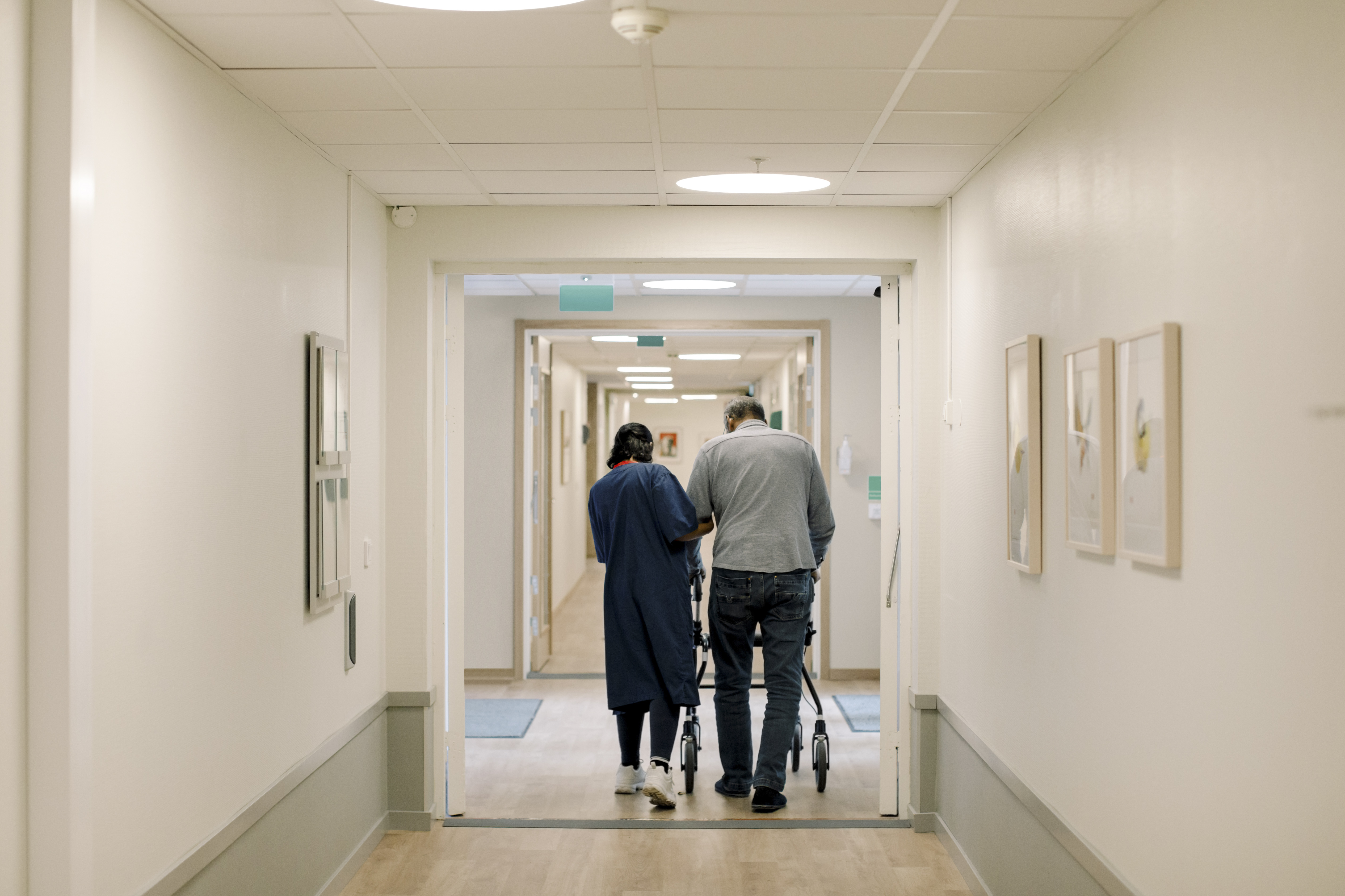 En vårdpersonal hjälper en patient med en rollator när de går i en korridor på ett medicinskt center.