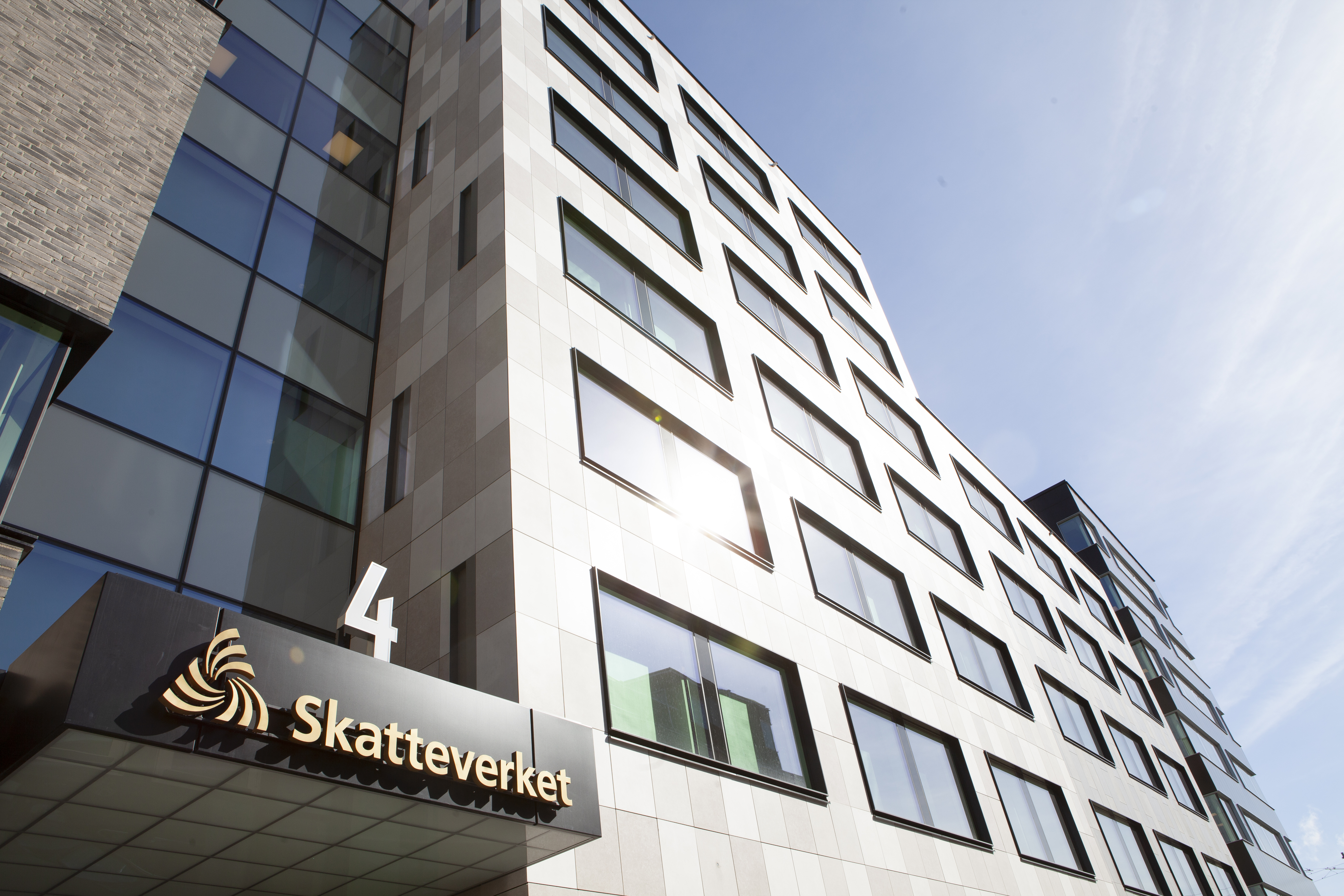 Kontorsbyggnad med stora fönster och en skylt med texten "Skatteverket" ovanförför ingången, fotad från låg vinkel.