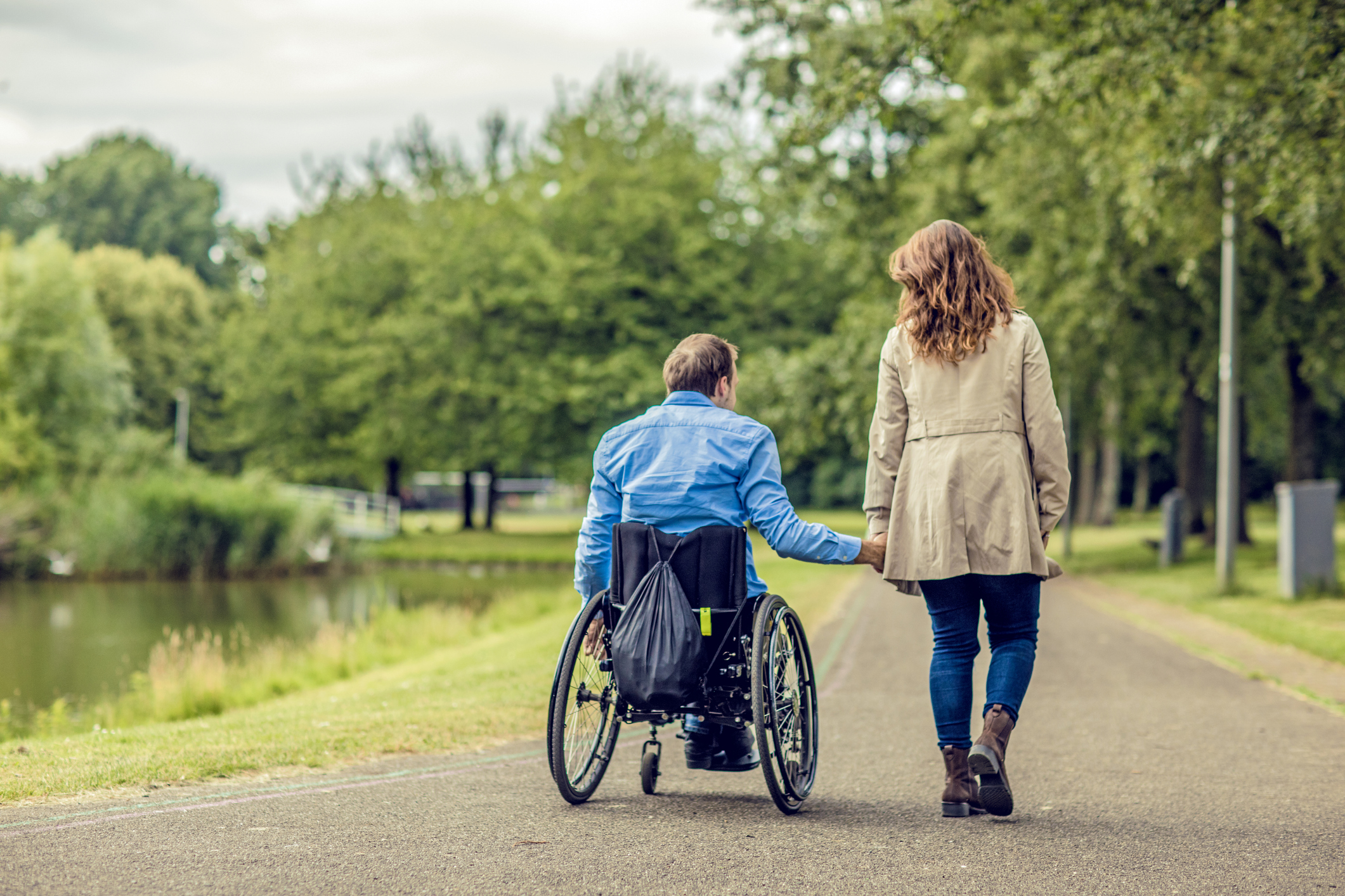 Wheelchair using young man and his girlfriend walking together through a city park on a sunny afternoon