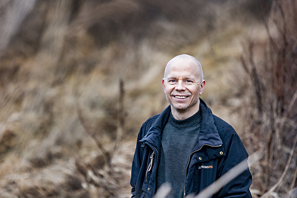 Profilbild på Lasse Mattila rakt framifrån. Han står utomhus, omgiven av vass