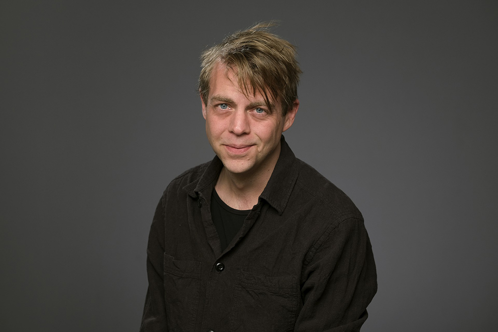 Porträtt av kriminologen Christoffer Carlsson i halvprofil framför en neutral bakgrund i grått.