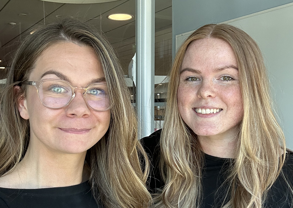 Porträttbild på socionomstudenterna Fanny Peltola och Nataniele Mickute, ståendes bredvid varandra utanför en universitetssal.