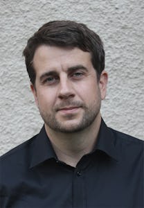 Porträtt på Joar Guterstam, ansikte och axlar, med grå neutral bakgrund.