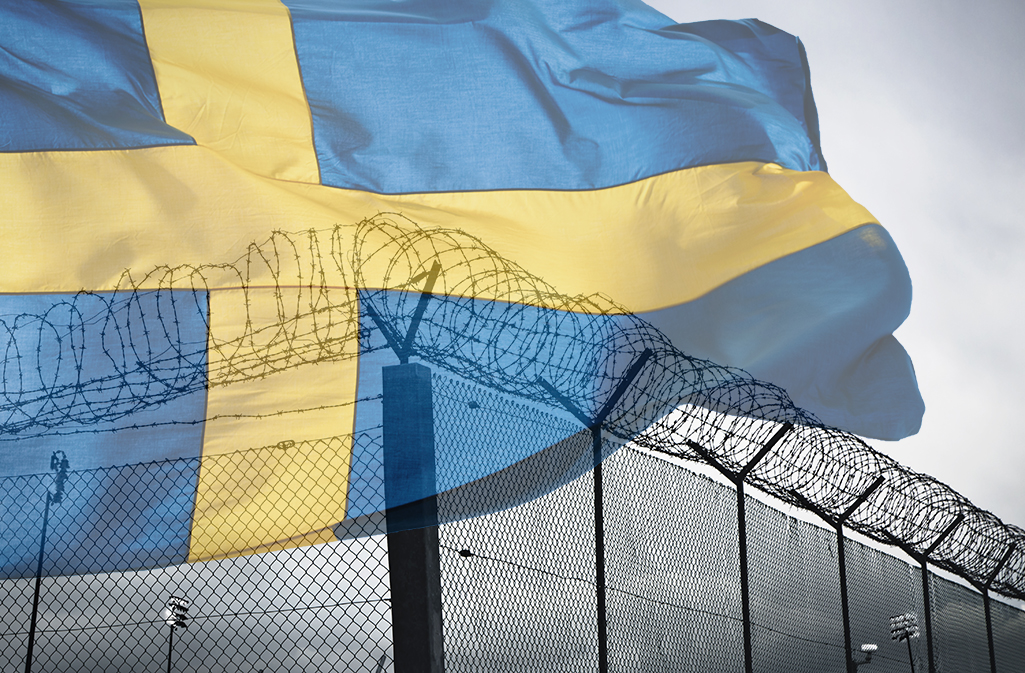 Stor svensk flagga vajar över ett stängsel med taggtråd.