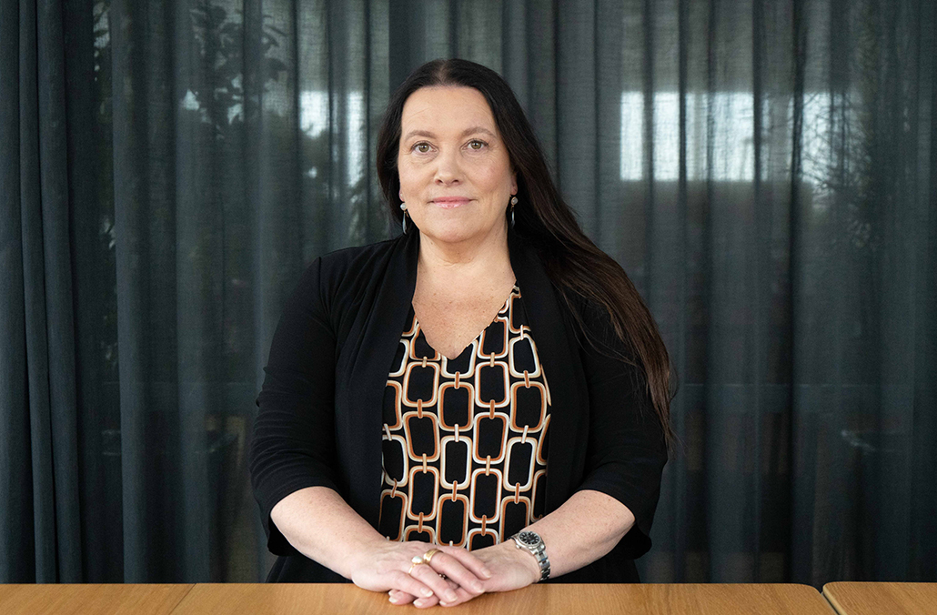 Porträttbild på juristen Monica Crusner i halvprofil, ståendes bakom ett bord.