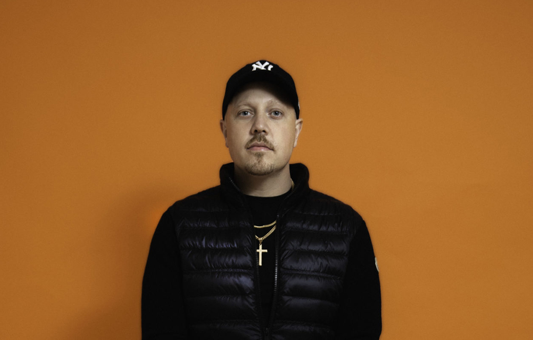 Porträttbild på Sebastian Stakset i halvprofil rakt framifrån, bakom en orange bakgrund