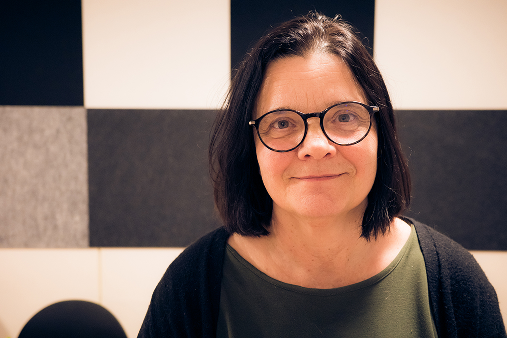 Porträttbild på forskaren Niki Sundström i halvprofil, ståendes framför schackmönstrad vägg.