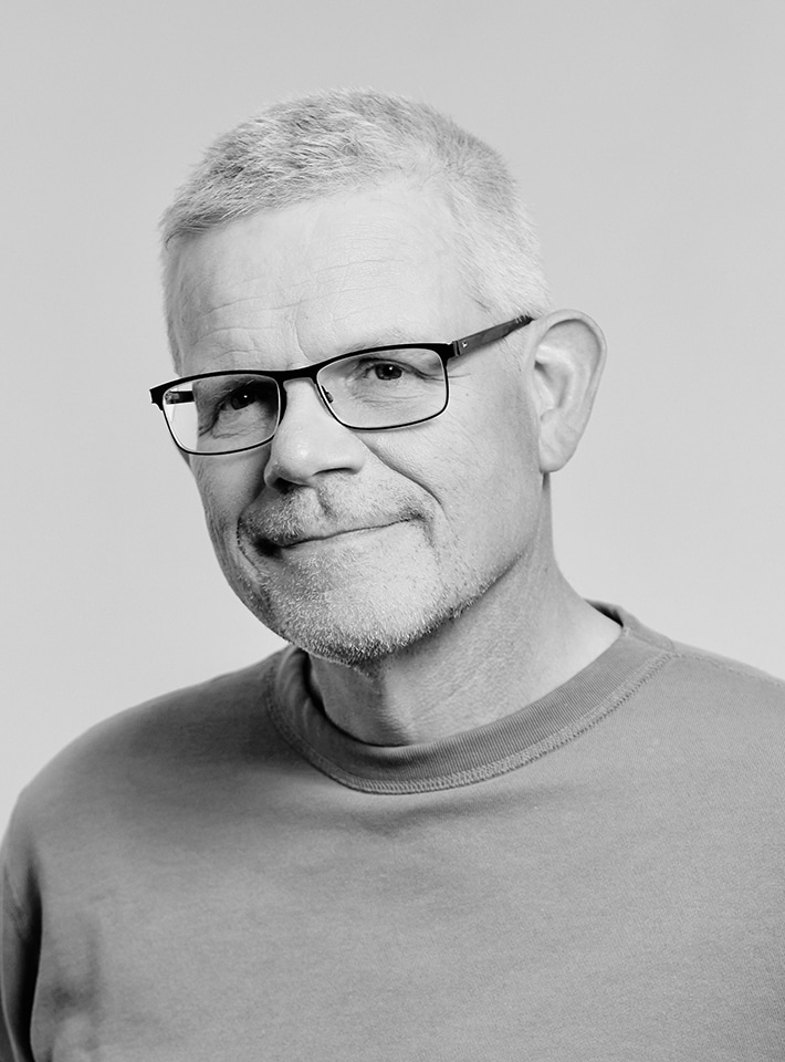 Porträttbild på Ernst Dahlquist i svartvitt, huvud och axlar, ståendes framför en helgrå bakgrund.