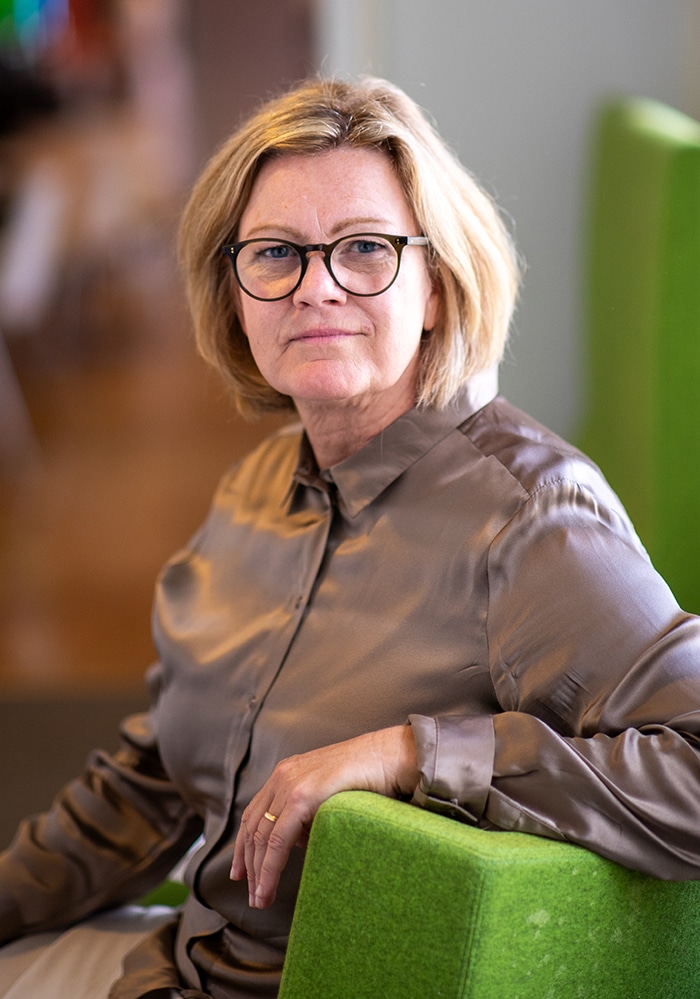 Halvporträtt på Yvonne Thilander, sittandes i en grön fåtölj framför ett suddigt kontorslandskap