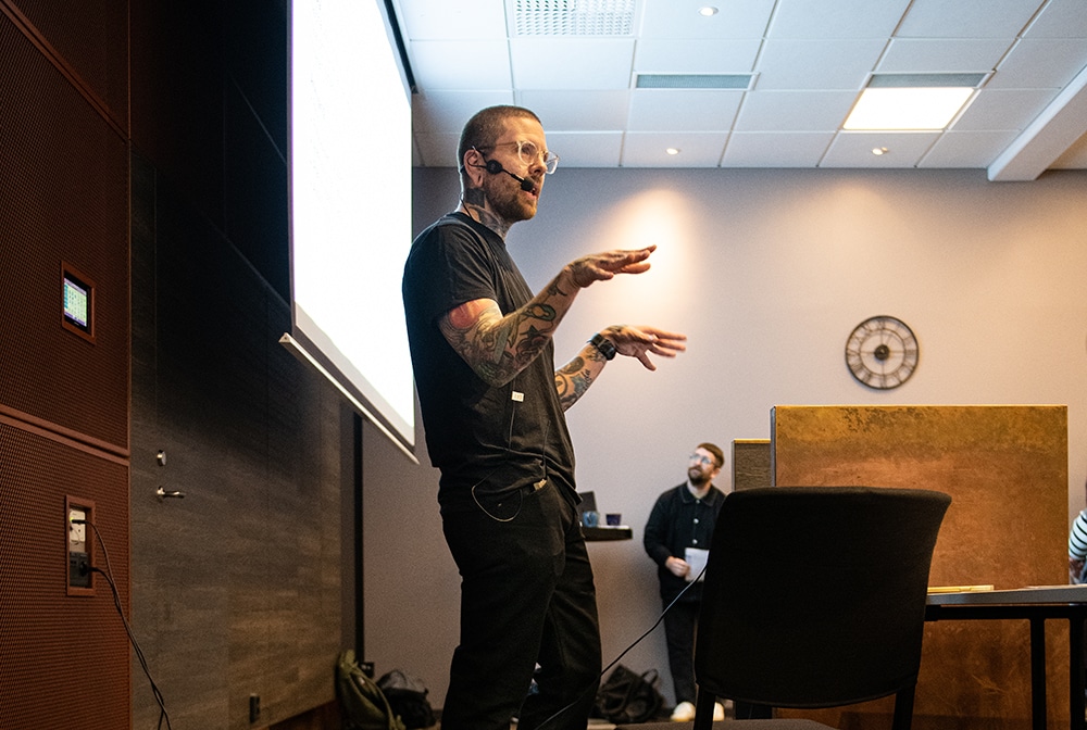 David Freundt, processledare i Grums kommun, står på en scen i en konferenslokal framför en står digital skärm.