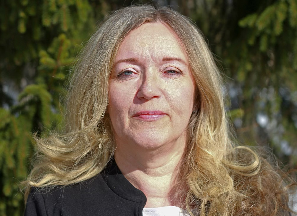 Porträtt på Carin Johansson, huvud och axlar, ståendes framför ett buskage.