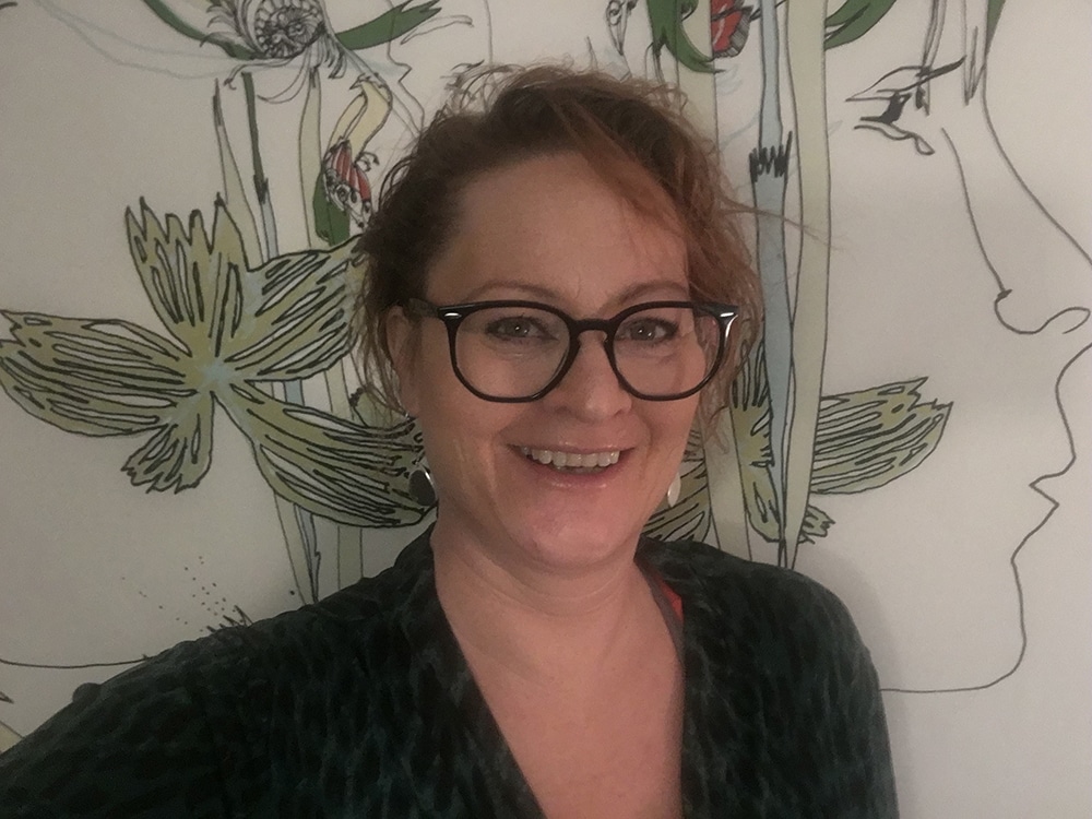 Porträttbild på Karolina Håkansson, huvud och axlar, ståendes framför vit gardin med blomstermotiv.