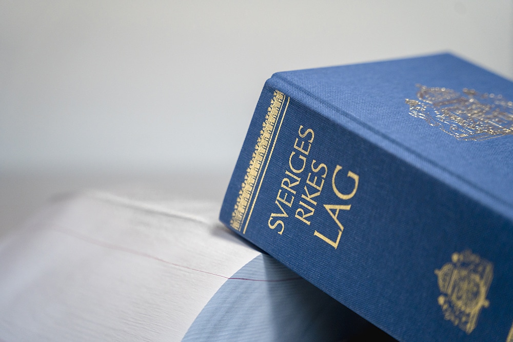 Den svenska lagboken ligger och vilar på en uppfälld bok vars titel och innehåll inte syns.